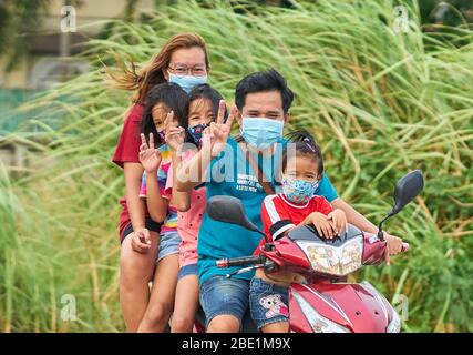 Una famiglia tailandese che viaggia su una moto, tutte indossando maschere facciali protettive, prese a Pathumthani, Thailandia, nel mese di aprile 2020. Foto Stock