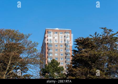 Alto blocco di appartamenti che torreggia su Southend sul lungomare del mare in un giorno soleggiato con cielo blu. Appartamenti Tower Court a Westcliff, attraverso gli alberi. Persone Foto Stock