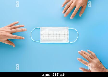 Mani che raggiungono fuori per ottenere maschera medica del viso per proteggere da germi e virus durante la situazione pandemica Foto Stock