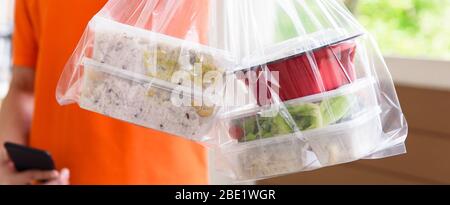 Immagine panoramica banner di scatole alimentari asiatiche in sacchetti di plastica consegnati al cliente a casa da uomo di consegna Foto Stock