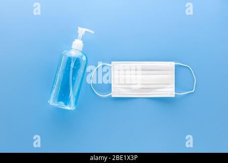 Maschera medica bianca e igienizzatore per mani con gel imbevuto di alcool per proteggere da virus e vista dall'alto su sfondo blu Foto Stock