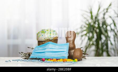 Torta di Pasqua, maschera protettiva viso medico, uova di cioccolato e coniglio, primo piano. Protezione contro i virus. Il concetto della celebrazione del Santo Foto Stock