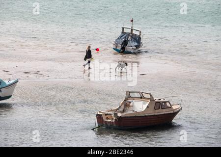 Donna che cammina un cane tra le barche sulla spiaggia, Margate Harbour, Kent, UK Foto Stock