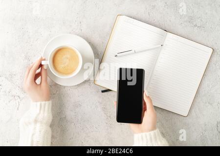Belle mani da donna con smartphone aggiornato e scrittura in blocco note con tazza di caffè su sfondo concreto. Concetto di business femminile. COFF Foto Stock