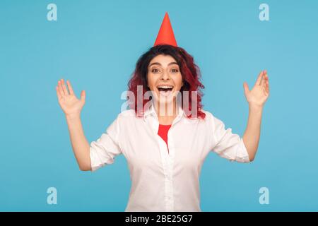 Eccitato stupito estremamente felice donna con il cono divertente partito sulla testa che solleva le mani, urlando gioiosamente con ammirazione, reazione emotiva al compleanno s Foto Stock