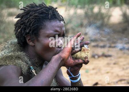 Hadzabe uomo fumo da un tradizionale tubo di argilla fotografato vicino al lago Eyasi, Tanzania Africa Foto Stock