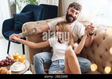 Immagine della romantica coppia compiaciuta che rende divertente e avvolgente mentre si fa colazione in sala luminosa a casa Foto Stock