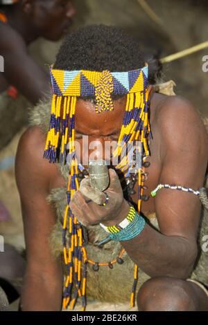 Hadzabe uomo fumo da un tradizionale tubo di argilla fotografato vicino al lago Eyasi, Tanzania Africa Foto Stock