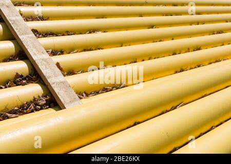 I tubi del gas naturale e i gasdotti sono impilati in un cantiere coperto da foglie cadute Foto Stock