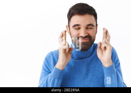 Ritratto ravvicinato di uomo bearded felice e sognante caucasico, occhi chiusi e sorridente ottimista come le dita incrociate buona fortuna, fare desiderio, ancipazione Foto Stock