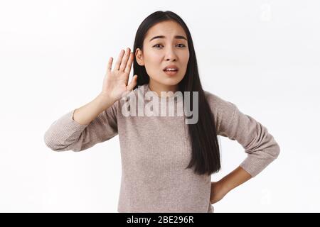 Parla più forte, non puoi sentirti. Perplesso e interrogato incerto est-asiatico donna non ha interferito che cosa è stato detto, tenere la mano vicino all'orecchio a eavesdrop, gossiping Foto Stock