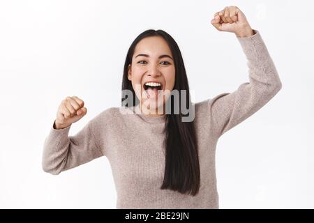 Allegra ragazza asiatica eccitata che ruggiva per la squadra di calcio, alzando le mani, pompa e sorridendo, grida di adorazione e brivido, devoted fan vogliono vincere Foto Stock