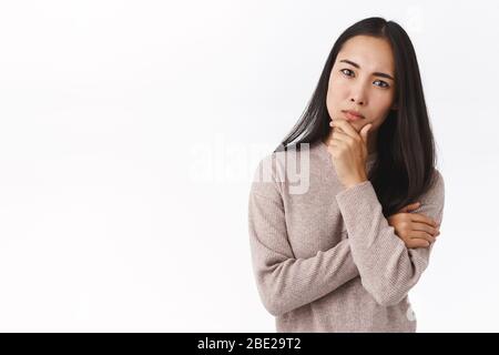 Ragazza bisogno seriamente pensare alla vostra offerta. Messa a fuoco giovane donna asiatica occupata collega, mento che tocca pensieroso, accigliato come guardando rigoroso, concentrato Foto Stock