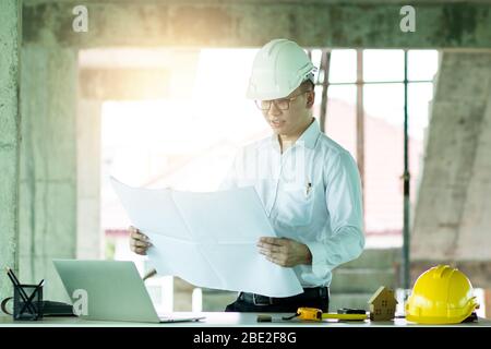 Ingegnere intelligente che guarda su stampa blu e verifica l'avanzamento dei lavori nel cantiere Foto Stock