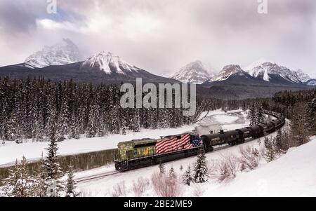 Un treno merci canadese del Pacifico a Morant's Curve in inverno lungo il fiume Bow sulla Bow Valley Parkway vicino Banff, Alberta, Canada Foto Stock