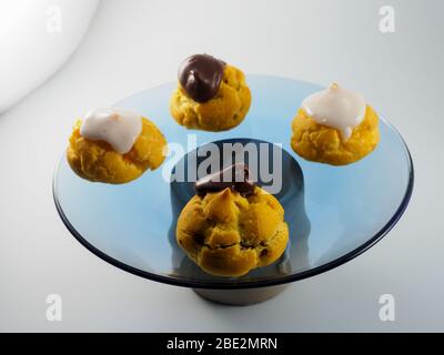 Quattro Profiterolle con crema e cioccolato su una piastra trasparente Foto Stock