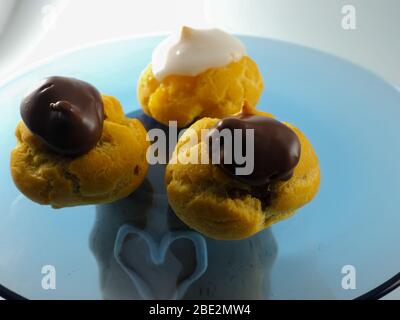 Tre Profiterolle con crema e cioccolato su una piastra trasparente Foto Stock