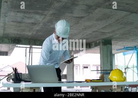 Business, edilizia, industria, tecnologia e concetto di persone, giovane ingegnere che lavora con taplet e laptop su tavolo in legno in cantiere, enginee Foto Stock