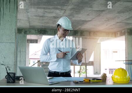 Ingegnere che lavora con taplet e laptop su tavolo in legno in cantiere, concetto di tecnologia ingegneristica Foto Stock