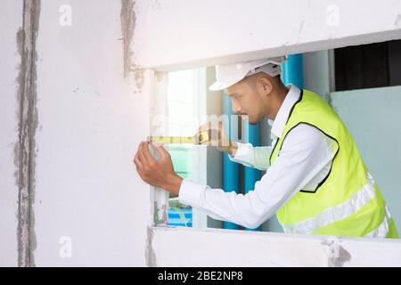 L'ispettore delle costruzioni controlla lo standard di spessore utilizzando il nastro di misurazione nell'edificio Foto Stock