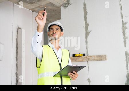 Ispettore che tiene appunti aprire carta e controllare l'edificio per la ristrutturazione, ingegnere topografo che cerca nel cantiere Foto Stock