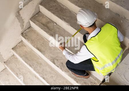 Ispettore che controlla l'edificio della larghezza della scala per eventuali lavori di ristrutturazione, ingegnere topografo che cerca nel cantiere. Concetto di consulenza per ispezione domestica Foto Stock