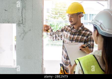 ispettore che controlla e misura con nastro di misurazione con assistente in cantiere Foto Stock