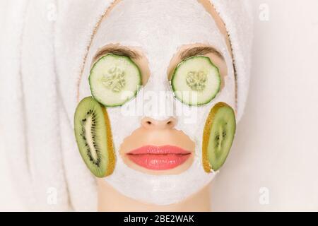 Cura della pelle e cosmetologia concetto. Vista dall'alto, primo piano di donna con maschera di fango argilloso sul viso, con fette di kiwi su guance e pezzi di cetriolo Foto Stock