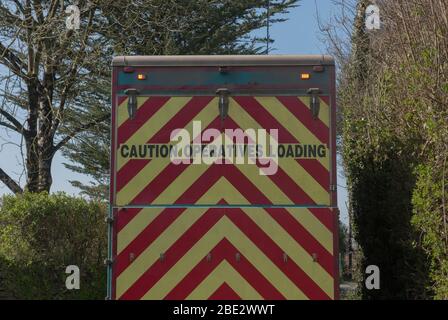 "Attenzione operatori Caricamento" segno sul retro di un camion di riciclaggio su un stretto Country Lane in un villaggio in Devon Rurale, Inghilterra, Regno Unito Foto Stock