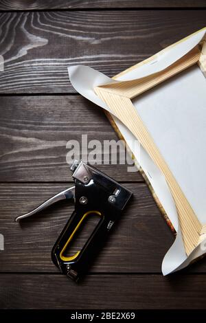 Tela che si allunga su barra di legno. Foto stampata su tela (vista posteriore) e pinzatrice su tavolo di legno marrone, vista dall'alto Foto Stock