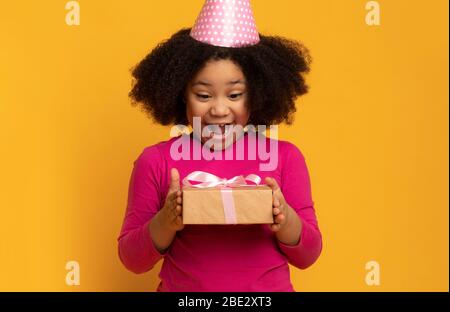 Sorpresa di compleanno. La ragazza nera overjoyed piccola in regalo di tenuta del cappello del partito Foto Stock