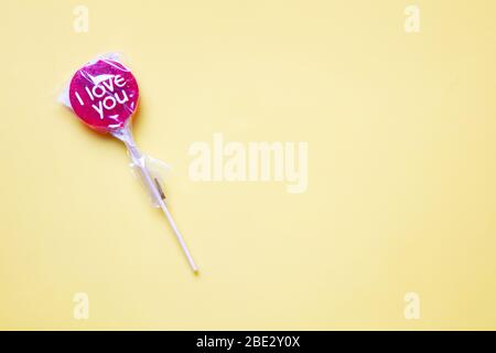 Un dolce lollypop rosso avvolto 'i Love You' su uno sfondo giallo pastello Foto Stock