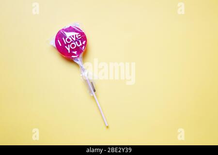 Un dolce lollypop rosso avvolto 'i Love You' su uno sfondo giallo pastello Foto Stock