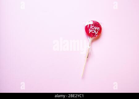 Un dolce lollypop rosso avvolto 'i Love You' su uno sfondo giallo pastello, piatto, vista dall'alto, minimalista Foto Stock