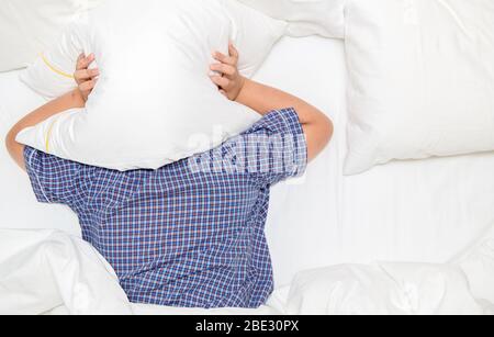 Ragazzo grasso obeso sdraiato sul letto coprendo la testa con cuscino perché troppo forte fastidioso rumore. Il bambino irritato che soffre dai vicini rumorosi, provando a dormire Foto Stock