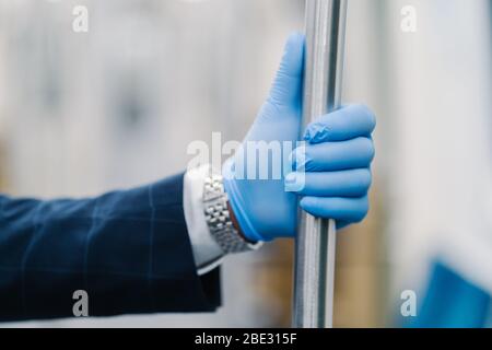 Uomo mano in guanto blu monouso toccando corrimano nei trasporti pubblici. Precauzioni pandemiche. Protezione contro virus e batteri. Coronavirus AN Foto Stock