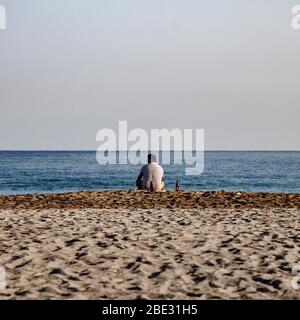 Un uomo che medita davanti al mare all'alba Foto Stock