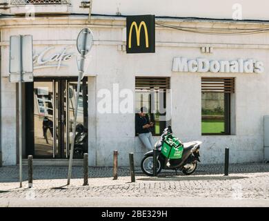 Cascais, Portogallo - 11 aprile 2020: Corrieri di consegna di Glovo e UberEats in moto di fronte ad un ristorante McDonalds durante il Coronavirus Covid- Foto Stock