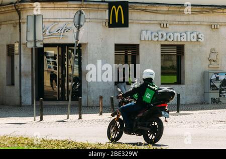 Cascais, Portogallo - 11 aprile 2020: Corrieri di consegna di Glovo e UberEats in moto di fronte ad un ristorante McDonalds durante il Coronavirus Covid- Foto Stock