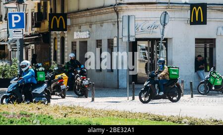 Cascais, Portogallo - 11 aprile 2020: Corrieri di consegna di Glovo e UberEats in moto di fronte ad un ristorante McDonalds durante il Coronavirus Covid- Foto Stock