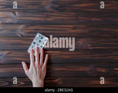 Blister con un'ultima pillola medicinale in mano di una donna su sfondo di legno. Concetto sanitario e medico. Telaio orisontale con spazio libero per Foto Stock