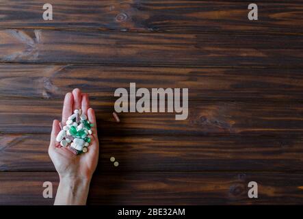 Un sacco di pillole colorate in mano di una donna su sfondo di legno. Concetto sanitario e medico. Cornice orisontale con spazio libero per il testo. Foto Stock