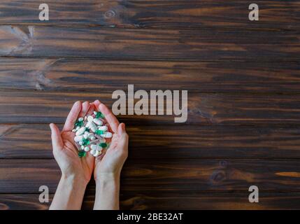 Molte droghe colorate nelle mani di una donna su sfondo di legno. Concetto sanitario e medico. Cornice orisontale con spazio libero per il testo. Foto Stock