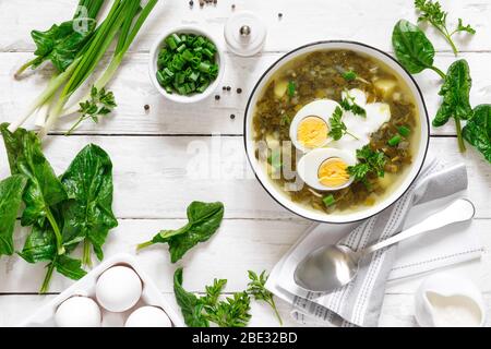 Zuppa verde di sorbetto e spinaci con uova bollite e panna acida su tavolo rustico in legno bianco, vista dall'alto Foto Stock