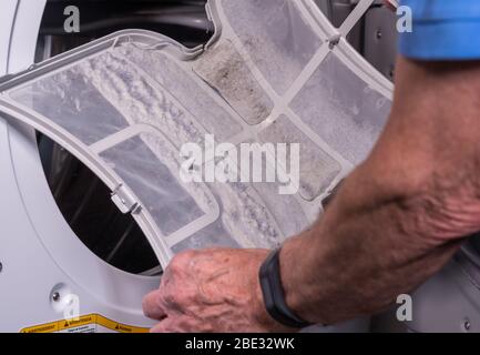 Uomo caucasico senior che trattiene la trappola piena di pelucchi da un essiccatore a tamburo a caricamento frontale Foto Stock