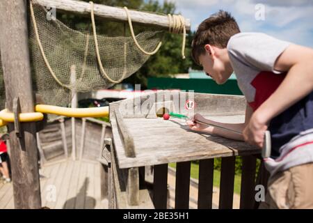 Un ragazzo di tredici anni si prepara a mettere una palla da golf in un tubo su un buco a tema nautico presso il campo di minigolf a Karlshagen, Germania. Foto Stock