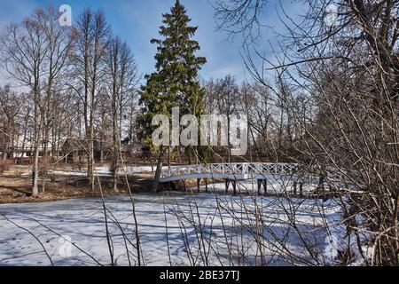 Un ponte con ringhiera in legno nella tenuta della famiglia Pushkin. Lo stagno è coperto di ghiaccio e neve. Il ponte ha una forma arcuata. Russia Foto Stock