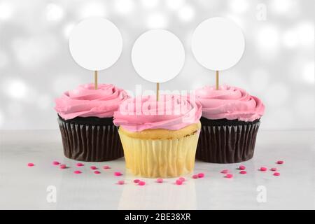 Tre cupcake gourmet con glassa rosa e spruzzate sedendosi tentevolmente su uno sfondo di marmo bianco. Foto Stock