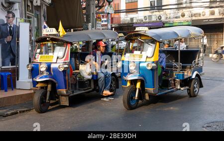 Bangkok, Thailandia - 28 Febbraio, 2020:due 'tuk-tuk' (il famoso taxi vecchio stile della Thailandia) autisti che prendono una pausa per una chiacchierata su una strada di Bangkok. Foto Stock