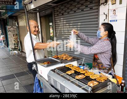 Bangkok, Thailandia - 28 febbraio 2020: Un tradizionale venditore di cibo di strada, che vende carne alla griglia su un bastone, in una strada di Bangkok. Foto Stock
